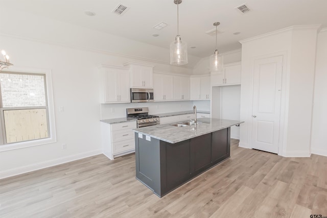 kitchen with stainless steel appliances, white cabinetry, sink, light stone counters, and an island with sink