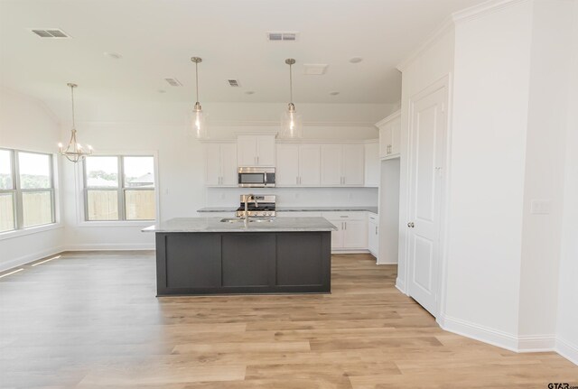 kitchen featuring white cabinets, hanging light fixtures, sink, a kitchen island with sink, and light hardwood / wood-style flooring