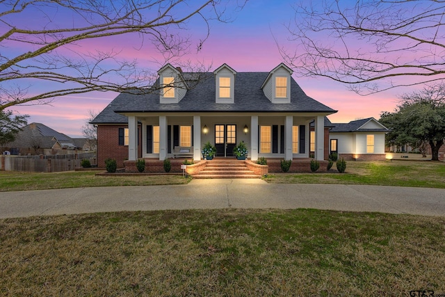 view of front of property with covered porch, brick siding, a shingled roof, fence, and a yard