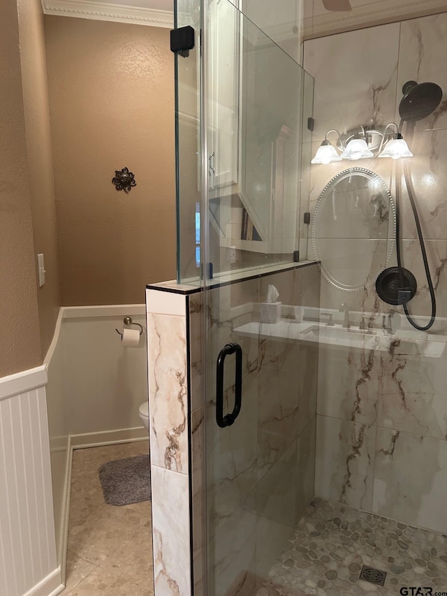 bathroom featuring toilet, ornamental molding, and a shower with shower door