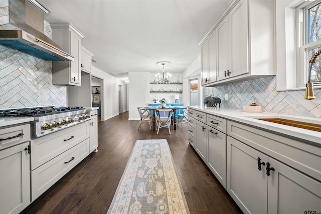 kitchen with stainless steel gas cooktop, light countertops, dark wood-style flooring, wall chimney exhaust hood, and a sink