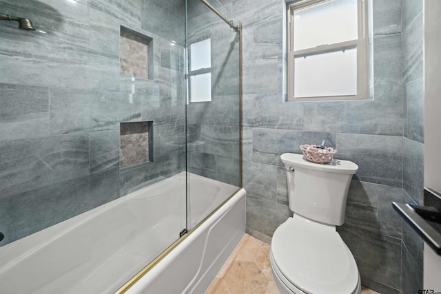 full bath featuring toilet, tile walls, and shower / bath combination with glass door