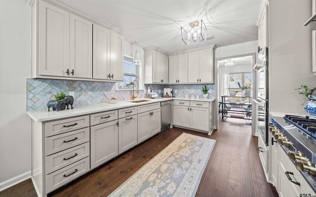 kitchen featuring dark wood finished floors, decorative backsplash, appliances with stainless steel finishes, a notable chandelier, and a sink