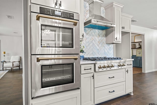 kitchen featuring visible vents, backsplash, appliances with stainless steel finishes, wall chimney exhaust hood, and light countertops