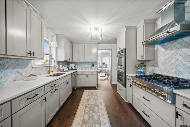 kitchen with a sink, stainless steel appliances, wall chimney exhaust hood, light countertops, and dark wood-style flooring