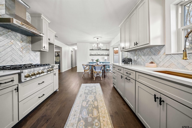 kitchen featuring a sink, wall chimney range hood, light countertops, dark wood-style flooring, and stainless steel gas cooktop