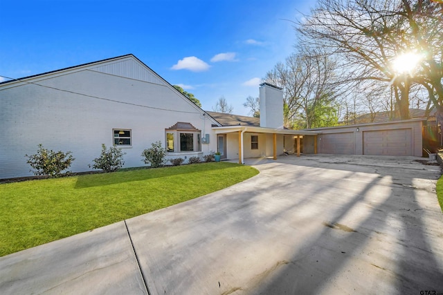 back of property featuring brick siding, a lawn, a chimney, and a garage