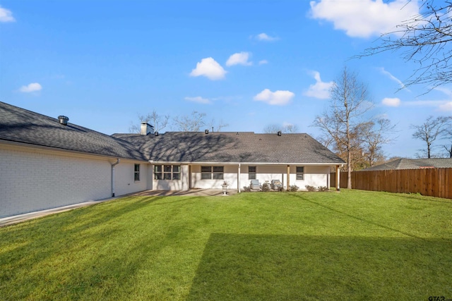 back of house featuring fence, roof with shingles, a chimney, a lawn, and brick siding