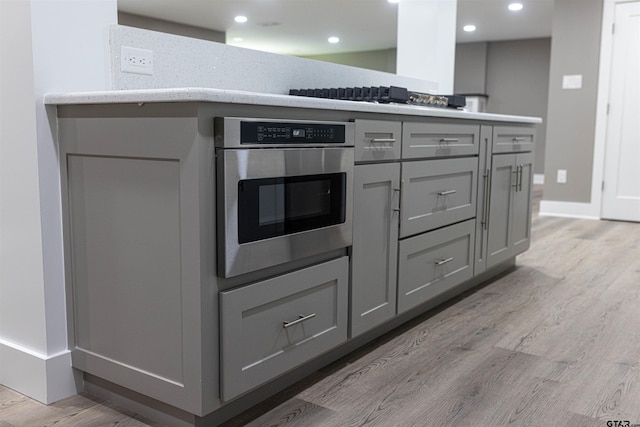 kitchen featuring light wood-style floors, baseboards, stainless steel oven, recessed lighting, and gray cabinets