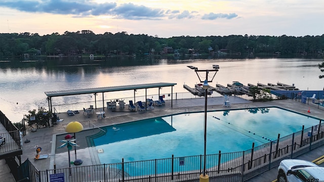 pool with a water view, a view of trees, a patio area, and fence