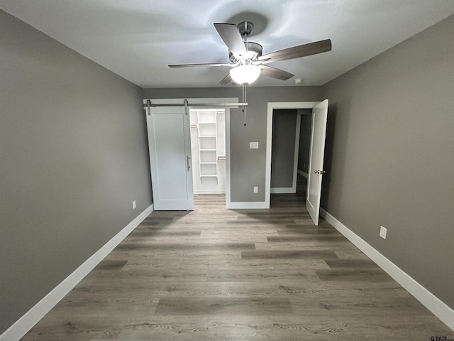 unfurnished bedroom with baseboards, a barn door, wood finished floors, and a spacious closet
