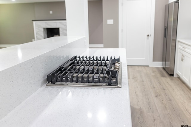 interior details with white cabinets, light stone counters, appliances with stainless steel finishes, a fireplace, and light wood-type flooring