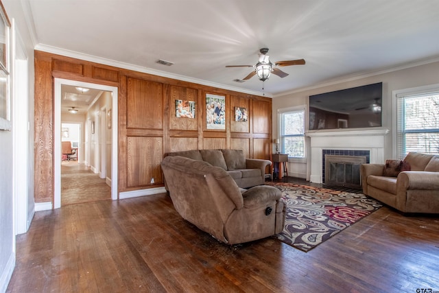 living room featuring visible vents, a ceiling fan, a glass covered fireplace, dark wood-style floors, and crown molding