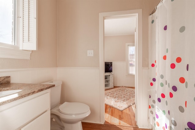 bathroom featuring a wainscoted wall, curtained shower, toilet, vanity, and wood finished floors