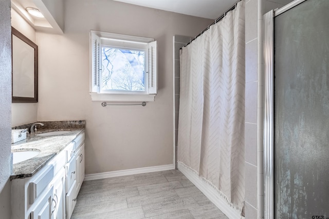 bathroom with double vanity, a shower with shower curtain, a sink, and baseboards