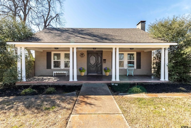 bungalow-style house featuring covered porch, brick siding, a chimney, and roof with shingles