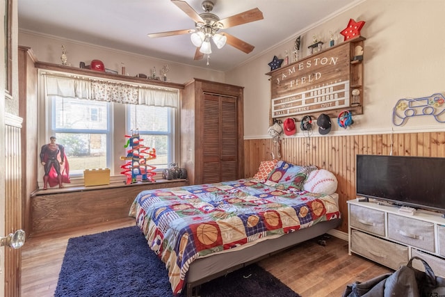 bedroom with a closet, light wood-style flooring, ornamental molding, wainscoting, and wood walls