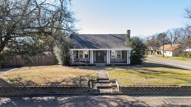 view of front of property featuring covered porch, a chimney, fence, and a front yard