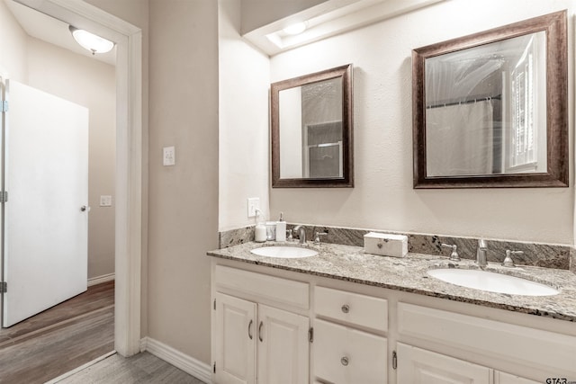 bathroom featuring wood finished floors, a sink, baseboards, and double vanity