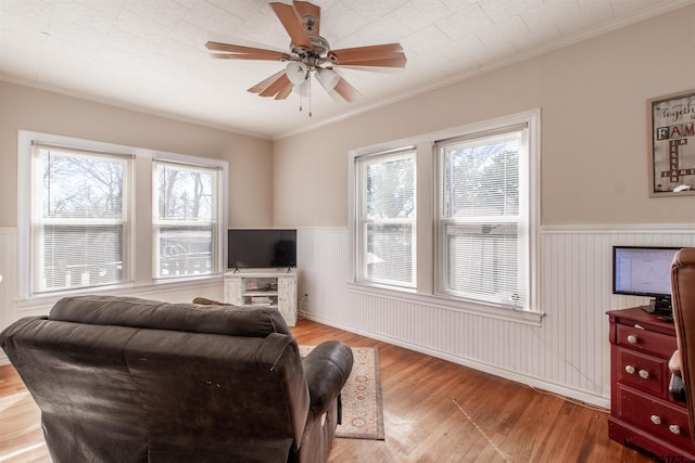 living area featuring a wainscoted wall, ceiling fan, ornamental molding, and wood finished floors