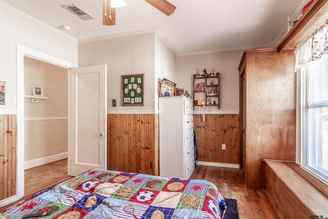 bedroom featuring a wainscoted wall, wood walls, wood finished floors, visible vents, and crown molding