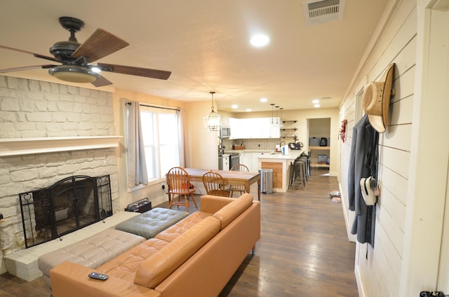 living room with ceiling fan, a stone fireplace, and dark wood-type flooring