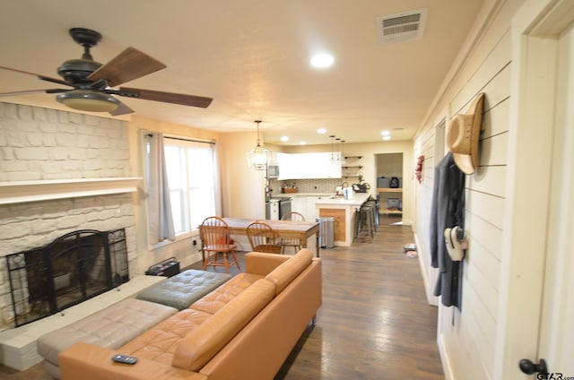 living room featuring a stone fireplace, dark wood-type flooring, and ceiling fan with notable chandelier