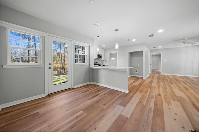 kitchen featuring white cabinetry, ceiling fan, kitchen peninsula, pendant lighting, and light wood-type flooring