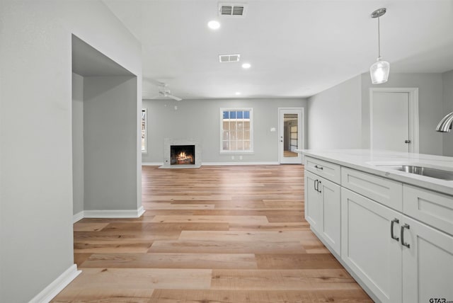 kitchen featuring light stone countertops, sink, light hardwood / wood-style flooring, white cabinets, and hanging light fixtures