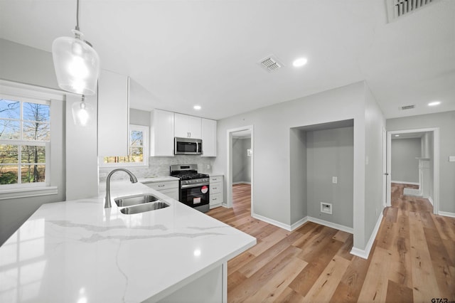 kitchen featuring appliances with stainless steel finishes, light stone counters, sink, pendant lighting, and white cabinets