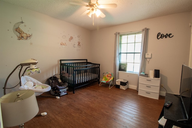 bedroom with dark wood-type flooring, ceiling fan, a textured ceiling, and a crib