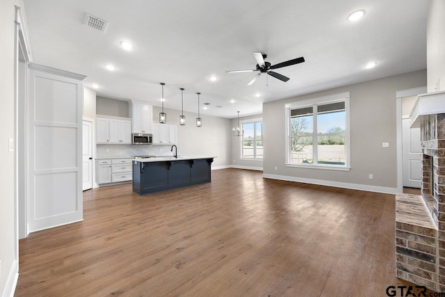 kitchen featuring white cabinetry, tasteful backsplash, an island with sink, a breakfast bar area, and pendant lighting