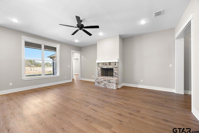 unfurnished living room with ceiling fan, a brick fireplace, and hardwood / wood-style floors