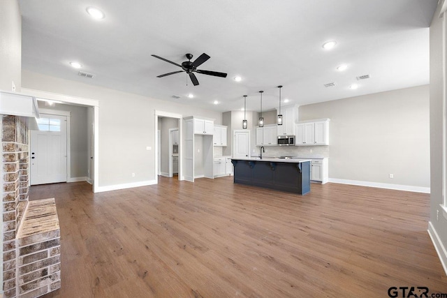 kitchen featuring an island with sink, pendant lighting, decorative backsplash, sink, and white cabinetry