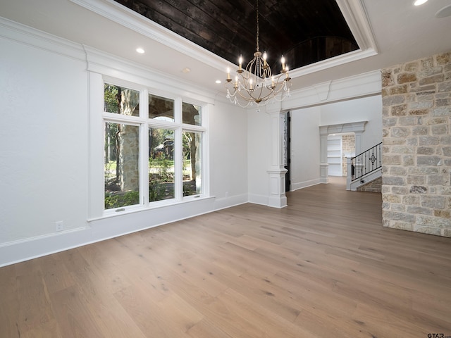 unfurnished dining area featuring a notable chandelier, hardwood / wood-style floors, a tray ceiling, and ornamental molding