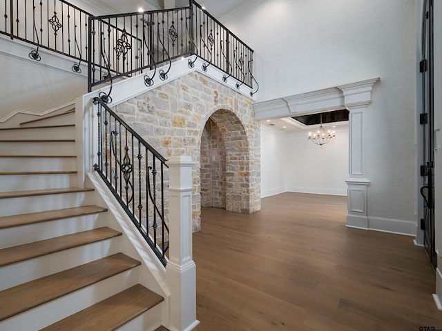 stairs featuring a notable chandelier, hardwood / wood-style flooring, ornamental molding, and decorative columns