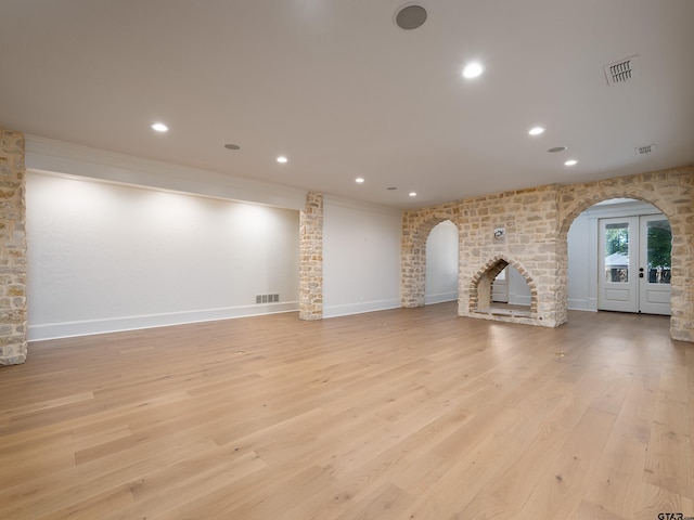 unfurnished living room featuring ornamental molding, a fireplace, light hardwood / wood-style floors, and french doors