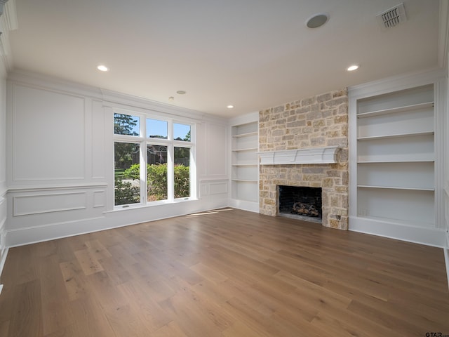 unfurnished living room featuring ornamental molding, hardwood / wood-style flooring, a stone fireplace, and built in features