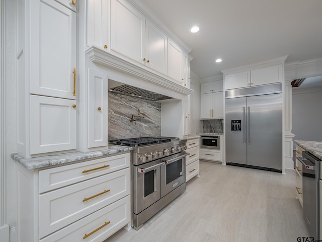 kitchen featuring white cabinetry, light stone countertops, backsplash, and premium appliances