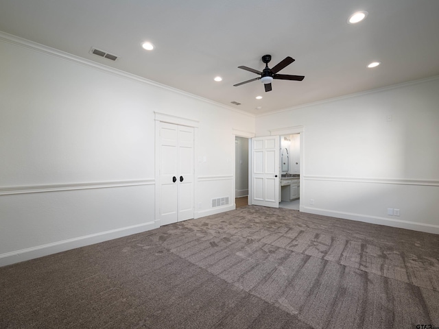 unfurnished bedroom with dark colored carpet, crown molding, ensuite bath, a closet, and ceiling fan