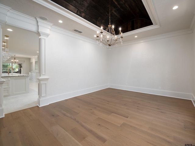 unfurnished dining area with crown molding, hardwood / wood-style floors, a tray ceiling, a chandelier, and ornate columns