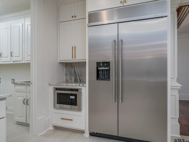 kitchen with stainless steel appliances, white cabinetry, tasteful backsplash, and light stone counters