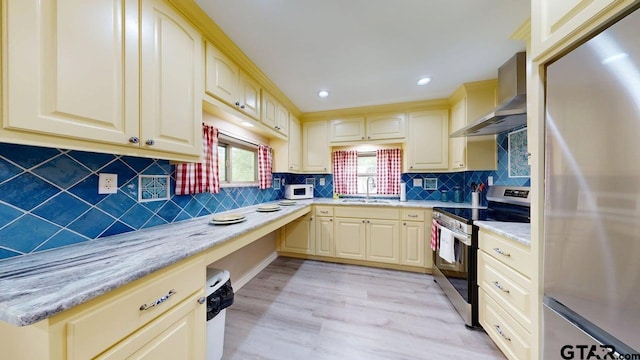 kitchen with built in study area, tasteful backsplash, stainless steel appliances, light wood-style floors, and wall chimney range hood