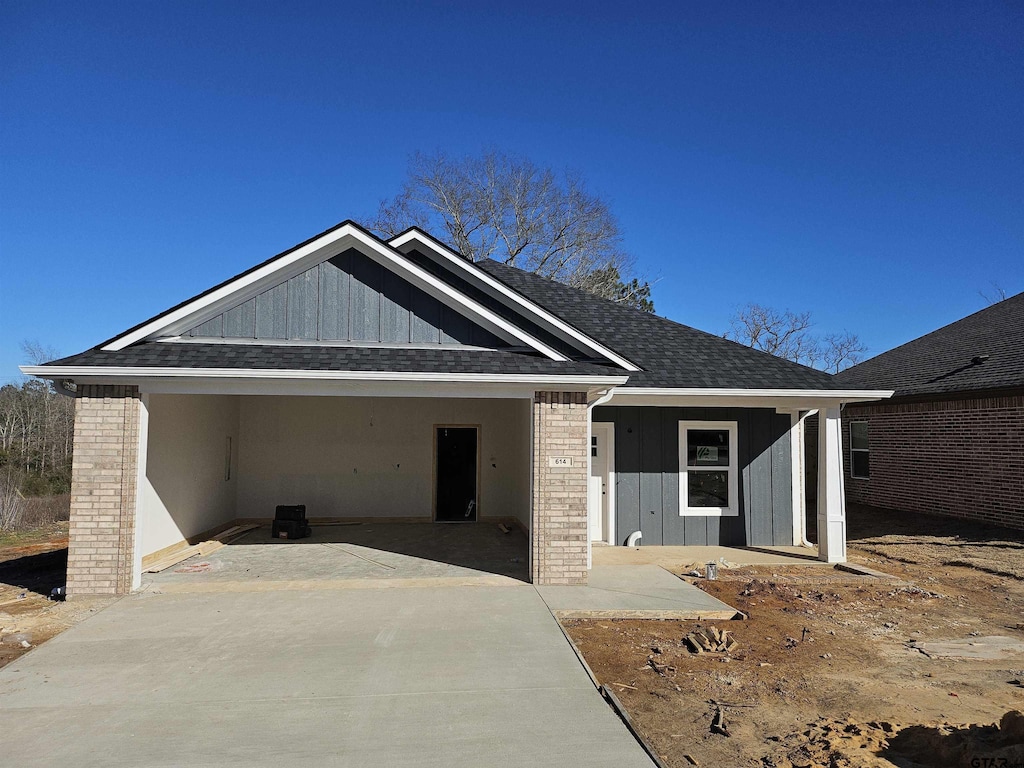 view of front of home with brick siding, a shingled roof, board and batten siding, a garage, and driveway