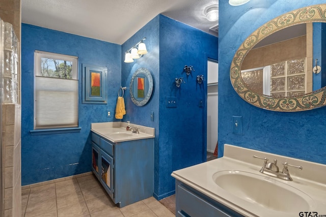 bathroom featuring tile patterned flooring, two vanities, a textured wall, and a sink