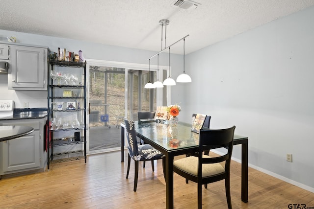 dining area with light wood-type flooring, visible vents, baseboards, and a textured ceiling