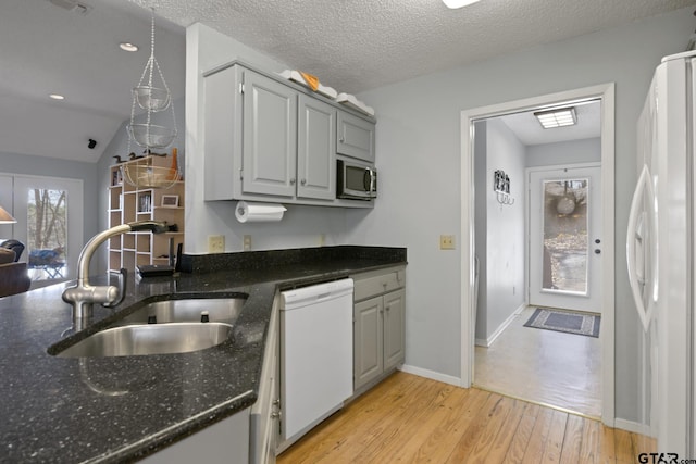 kitchen with light wood finished floors, dark stone counters, white appliances, a textured ceiling, and a sink