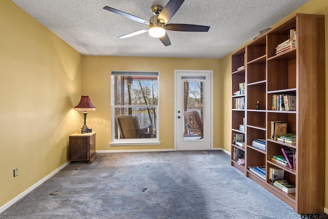 interior space with a textured ceiling, carpet, baseboards, and ceiling fan