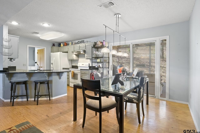 dining space featuring light wood-type flooring, visible vents, baseboards, and a textured ceiling