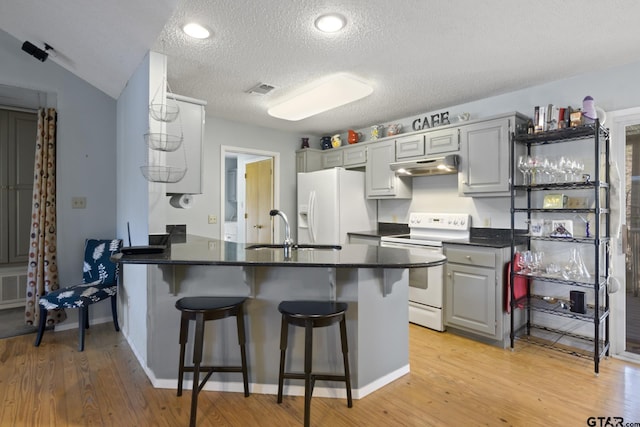 kitchen featuring under cabinet range hood, a sink, dark countertops, white appliances, and a peninsula